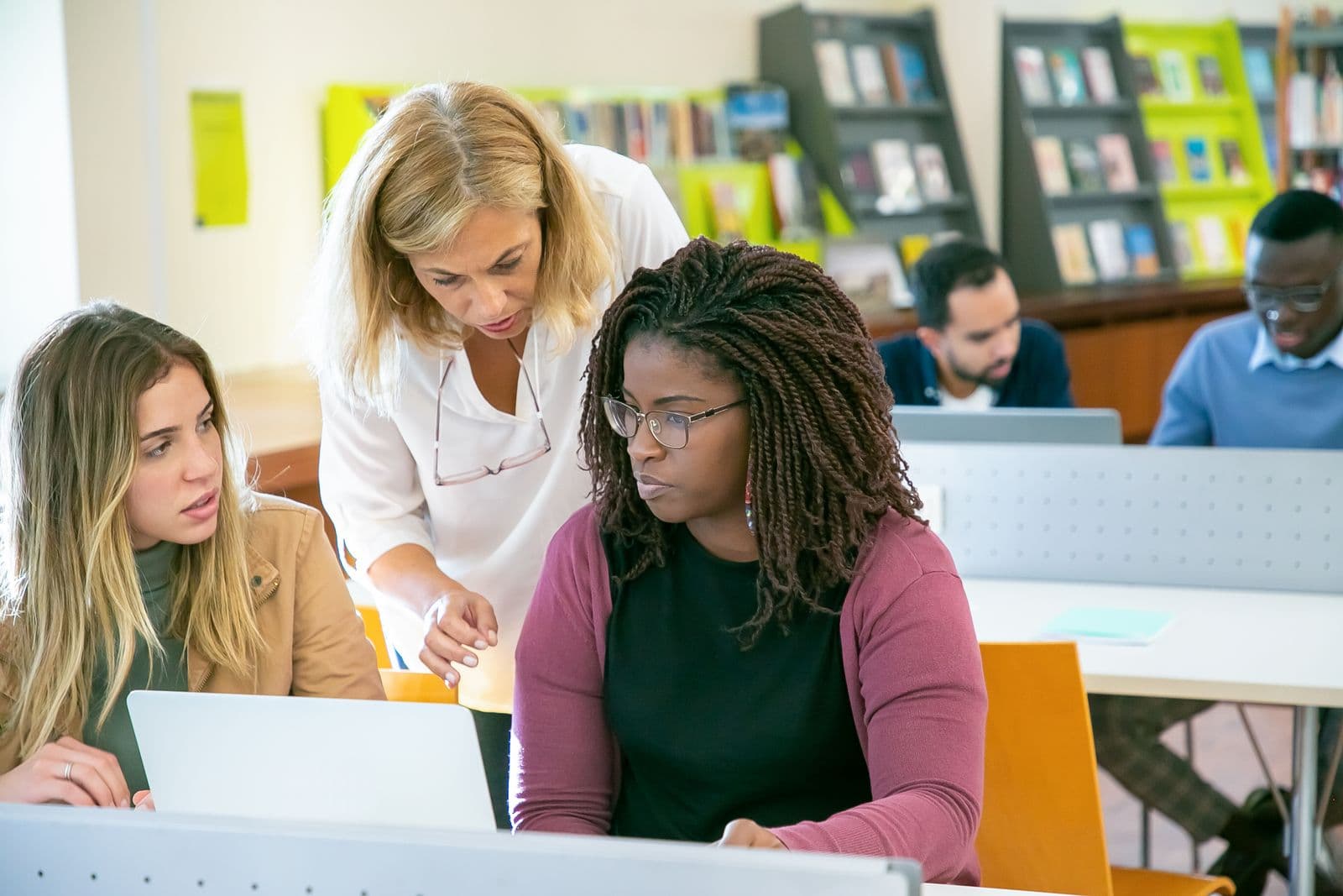 A mentor giving close, personalised feedback to a Black woman learner at a laptop, with other diverse learners alongside