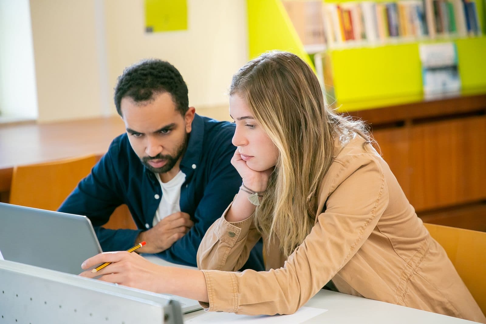 A Black practitioner and a learner working side by side at a laptop in a library
